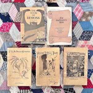 May include: A collection of vintage fantasy role-playing game books. Titles include "The Book of Demons," "The Spellcaster's Bible," and volumes of "The Arduin Grimoire." The books feature illustrations and text in a classic, aged style, with a variety of cover designs.