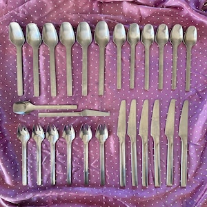 May include: A collection of stainless steel flatware including twelve spoons, six forks, six knives, and two additional serving utensils. The set features a simple, smooth design with straight handles and a polished metallic finish.