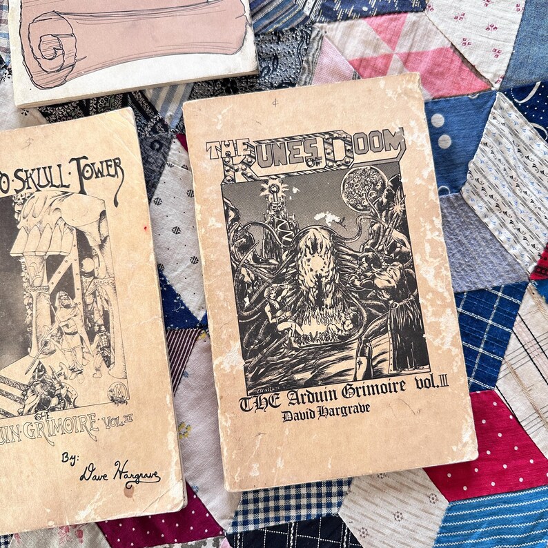Puede incluir: Libros de fantas&iacute;a vintage con ilustraciones en blanco y negro. Un libro se titula "The Dunes of Doom" y otro "Skull Tower". Los libros est&aacute;n sobre un edred&oacute;n de retazos colorido.