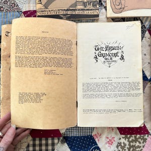 Puede incluir: Libro abierto con el t&iacute;tulo "The Arduin Grimoire Vol. II" en letras negras. Las p&aacute;ginas est&aacute;n amarillentas y el libro est&aacute; abierto para revelar texto. El libro est&aacute; sobre una superficie estampada.