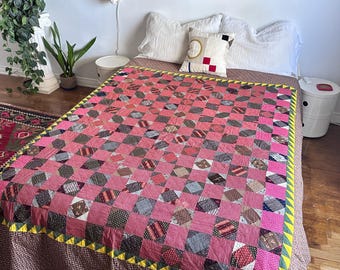 Pode incluir: Uma colcha de retalhos com uma grade de quadrados alternados cor-de-rosa e tecido estampado multicolorido. A colcha é contornada por um padrão triangular amarelo e verde e cobre uma cama com almofadas brancas e uma saia de cama castanha.