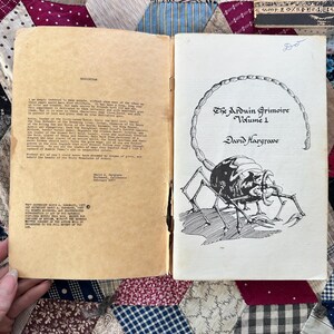 Puede incluir: Libro vintage abierto, titulado "The Arduin Grimoire Volume 1" de David Hargrave. La portada presenta una ilustraci&oacute;n en blanco y negro de una criatura parecida a un escorpi&oacute;n. P&aacute;ginas amarillentas.