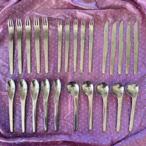May include: A collection of stainless steel flatware including five forks, five spoons, five knives, and five soup spoons. The set features a uniform metallic finish with slender handles and simple, functional shapes arranged in rows on a surface.