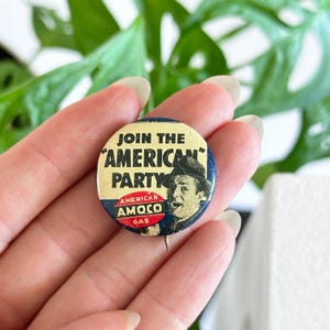 Puede incluir: Un botón vintage circular con el texto "JOIN THE AMERICAN PARTY" y una ilustración de un hombre. El botón también presenta las palabras "AMERICAN AMOCO GAS" en rojo y blanco.