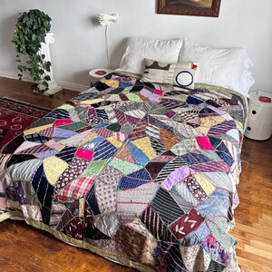 May include: A colorful patchwork quilt with a variety of fabric patterns and colors, including pink, blue, and green. The quilt is on a bed with white pillows and a decorative pillow with a blue circle design. The quilt's dimensions are not visible.