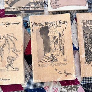 Puede incluir: Una colecci&oacute;n de libros antiguos con cubiertas de color beige envejecido. El libro central presenta el t&iacute;tulo "WELCOME TO SKULL TOWER" en una fuente g&oacute;tica, con ilustraciones de figuras y una torre. Otros libros incluyen "Arduin Grimoire".