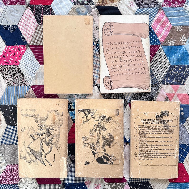 Puede incluir: Una colecci&oacute;n de libros antiguos con cubiertas desgastadas. Un libro presenta un dise&ntilde;o de pergamino con texto, mientras que otros muestran ilustraciones y texto. Los libros est&aacute;n dispuestos sobre un edred&oacute;n de retazos.