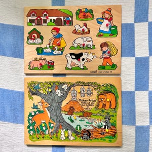 May include: Two wooden jigsaw puzzles. The top puzzle features farm animals and people. The bottom puzzle is a Fisher-Price puzzle with animals and the text "ANIMALS and their BABIES". Both puzzles are on a blue and white checkered surface.