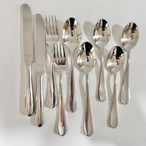 May include: A set of polished silverware, comprising knives, forks, and spoons, displayed on a white surface. The cutlery has a reflective, metallic finish, with elongated handles and a classic design. The set includes two knives, two forks, and five spoons.