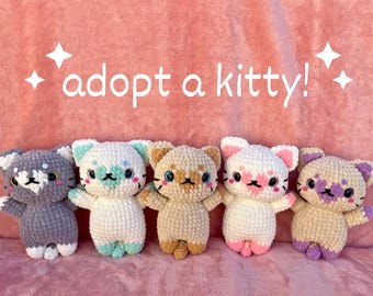 May include: Five handmade crochet cat plushies in various colors, including gray, white, and tan, with embroidered facial features. The text "adopt a kitty!" is displayed above the plushies on a pink background.