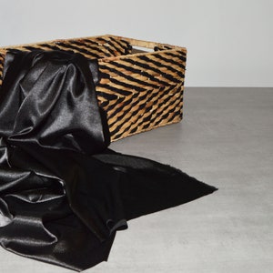 May include: A black satin fabric draped over a woven wicker basket with black accents.