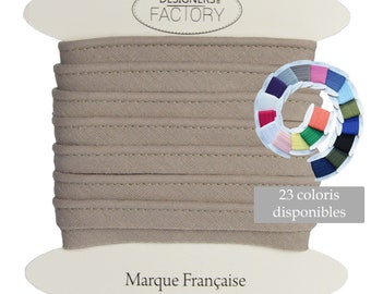 Könnte beinhalten: Eine Spule mit beigefarbenem Stoffbesatz mit einer genähten Kante. Der Besatz ist um eine weiße Karte mit dem Text "DESIGNERS® FACTORY" und "Marque Française" gewickelt. Eine Farbkarte zeigt 23 verschiedene Farben des Besatzes.