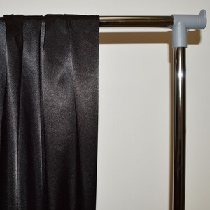May include: Black satin fabric draped over a silver metal clothing rack.
