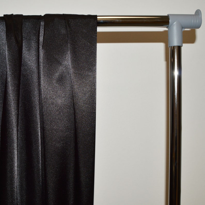 May include: Black satin fabric draped over a silver metal clothing rack.