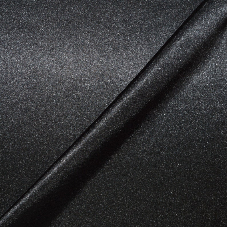 May include: A close-up of a black fabric with a subtle shimmer. The fabric is folded in half, creating a diagonal line across the image.