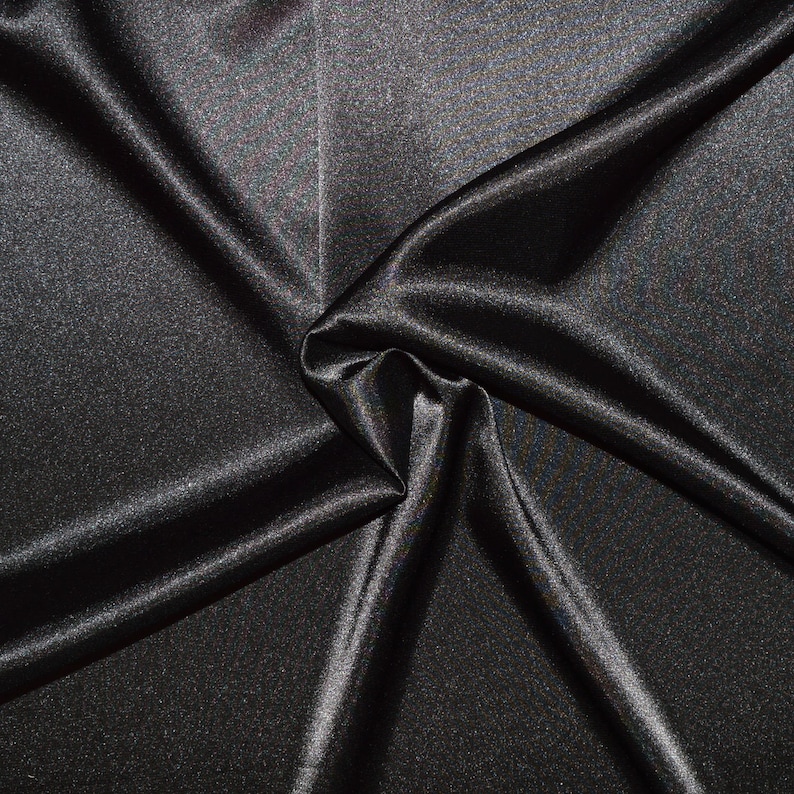 May include: Black satin fabric with a smooth, silky texture. The fabric is draped and folded, creating soft curves and folds.