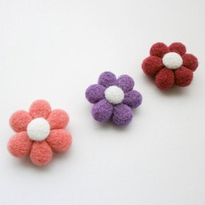May include: Three felt flower embellishments in pink, purple, and red with white centres.