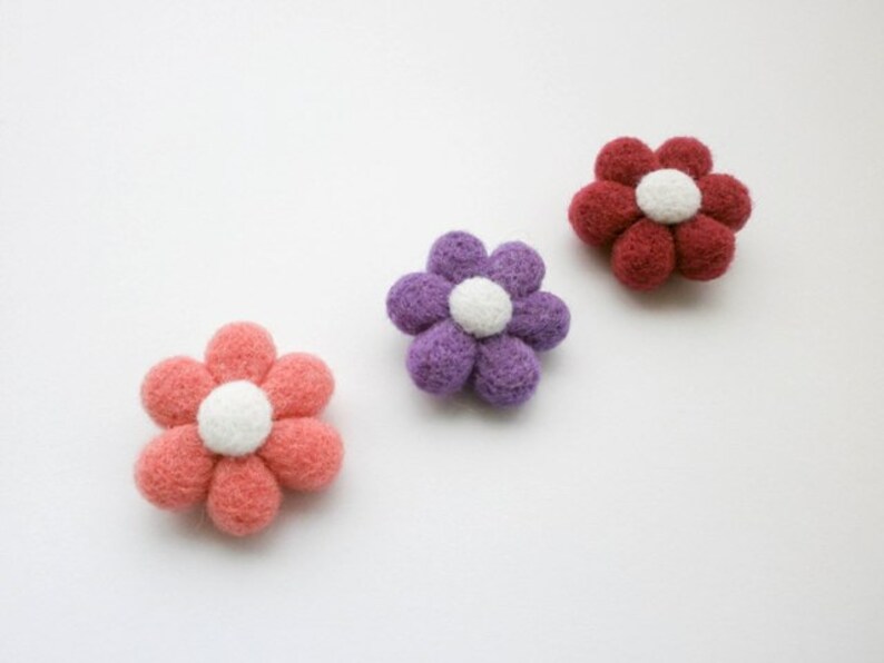 May include: Three felt flower embellishments in pink, purple, and red with white centres.