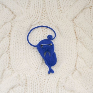May include: A blue felt animal brooch in the shape of a bird with a safety pin on the back.