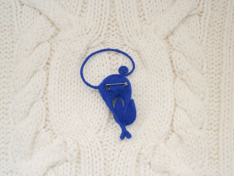 May include: A blue felt animal brooch in the shape of a bird with a safety pin on the back.