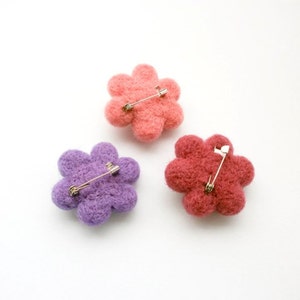 May include: Three felt flower brooches in pink, purple and red with silver safety pins attached to the back.