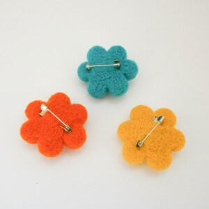 K&ouml;nnte beinhalten: Drei Filzblumenbroschen in T&uuml;rkis, Orange und Gelb. Jede Blume hat eine Sicherheitsnadel auf der R&uuml;ckseite.