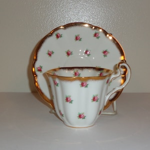 Puede incluir: Una taza de té y un platillo blancos con un borde dorado y un patrón de rosas rosas.