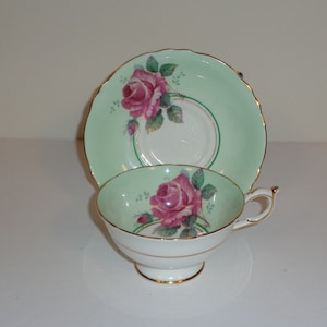 Może przedstawiać: Zestaw filiżanki i spodeczka do herbaty w stylu vintage z zielonym tłem i wzorem różowych róż.