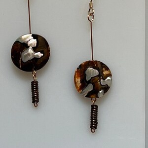 May include: A pair of gold dangle earrings with brown and white shell-like round pendants and brown metal beads hanging from the bottom.