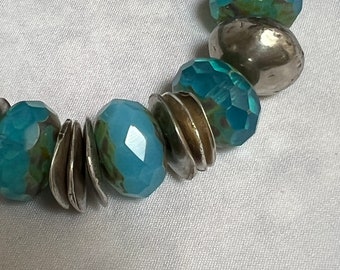 May include: A bracelet made of blue and silver beads. The beads are faceted and have a shimmery finish. The bracelet is made of a variety of materials, including glass and metal.