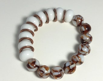 May include: A white and brown beaded bracelet with copper wire accents. The white beads are on one side of the bracelet and the brown beads are on the other side.