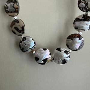 May include: A necklace made of round, brown, white, and black shell beads.