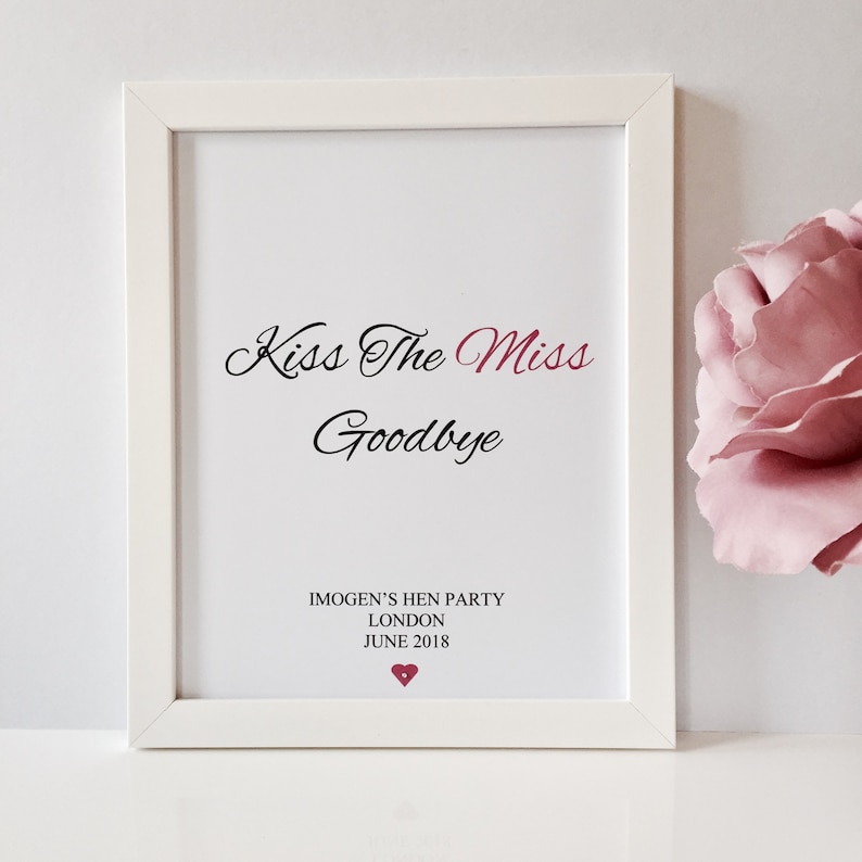 May include: White framed print with the text "Kiss The Miss Goodbye" in black cursive font. Below the text is "Imogen's Hen Party London June 2018" in black font. A small red heart is below the text.
