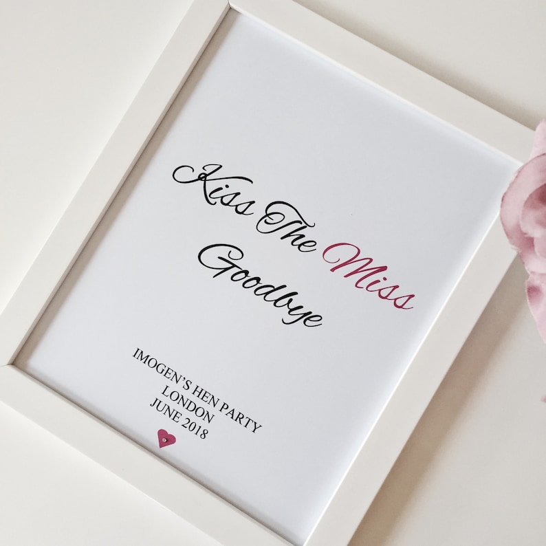 May include: White framed print with the text "Kiss The Miss Goodbye" in black cursive script. The word "Miss" is in pink. Below the text is "Imogen's Hen Party, London, June 2018" in black text. A small pink heart is below the text.