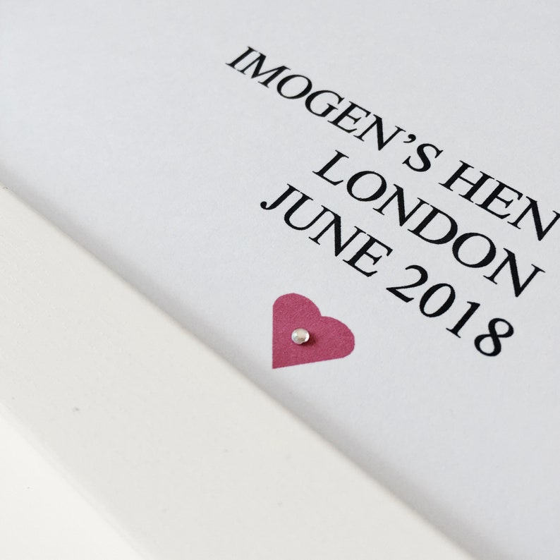 May include: A white card with black text that reads "Imogen's Hen London June 2018". A pink heart with a silver dot is in the bottom right corner.