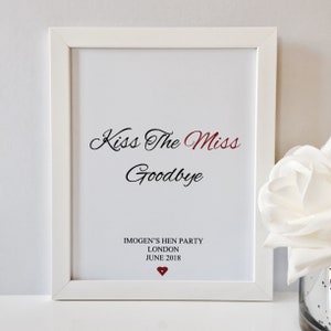 May include: White framed print with the text "Kiss The Miss Goodbye" in black cursive font. Below the text is "Imogen's Hen Party London June 2018" in black font. A small red heart is below the text.