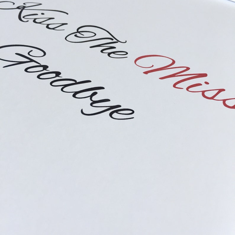 May include: White card with the text "Kiss the Goodbye Miss" written in black and red cursive.