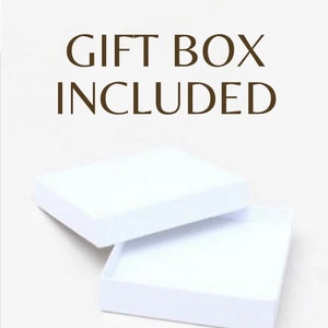 Może przedstawiać: Białe pudełko prezentowe z otwartą pokrywką. Tekst "GIFT BOX INCLUDED" jest nadrukowany brązowymi literami na białym tle.