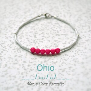 May include: A silver bracelet with pink beads spelling out "Ohio" in Morse code. The bracelet is on a white background.  -- / .... / .. / --