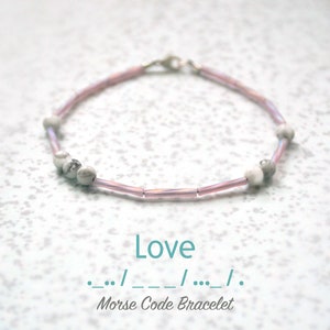 May include: A pink and white beaded bracelet with a silver clasp. The bracelet spells out the word "LOVE" in Morse code.