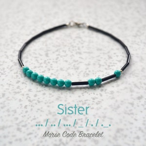 May include: A black and turquoise beaded bracelet with a silver clasp. The bracelet spells out "Sister" in Morse code.