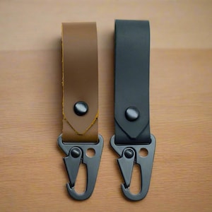 May include: Two leather keychains with black metal clips. One keychain is brown leather and the other is black leather.