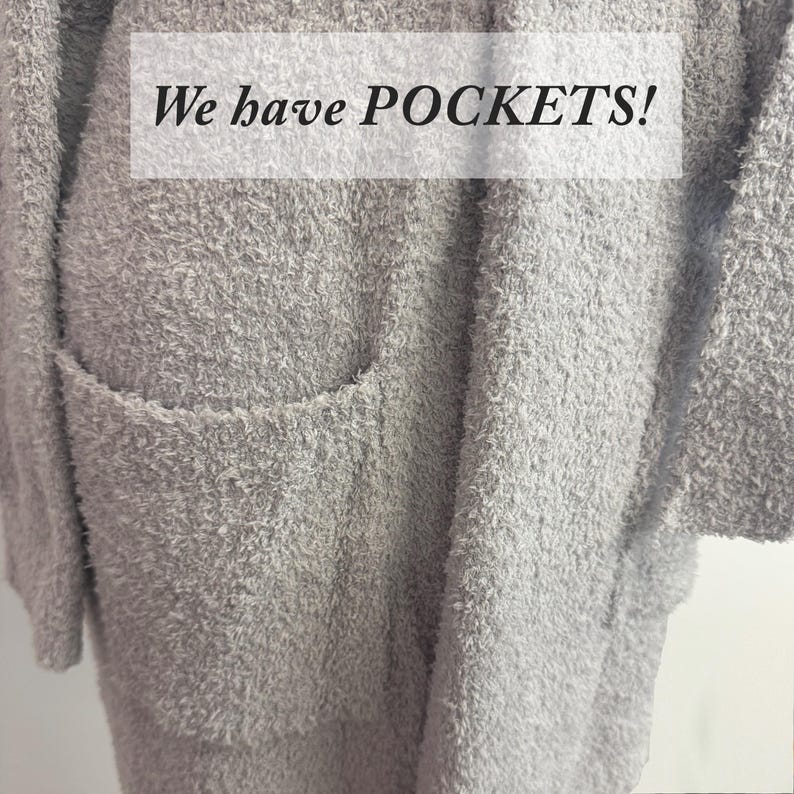 May include: A light gray, fuzzy cardigan with a large pocket is shown. The text "We have POCKETS!" is displayed in a white rectangle across the top of the image. The cardigan has a soft, textured appearance.