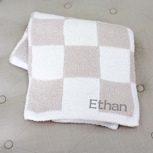 May include: A white and beige checkered baby blanket with the name "Ethan" embroidered on it.