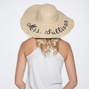 May include: A straw sun hat with a wide brim and black embroidery that reads "Mrs. Sullivan".
