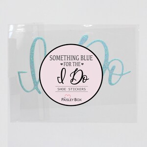May include: A clear plastic bag containing a pair of light blue glitter shoe stickers that say "I Do". The stickers are packaged with a pink and white circle sticker that says "Something Blue for the I Do Shoe Stickers The Paisley Box".