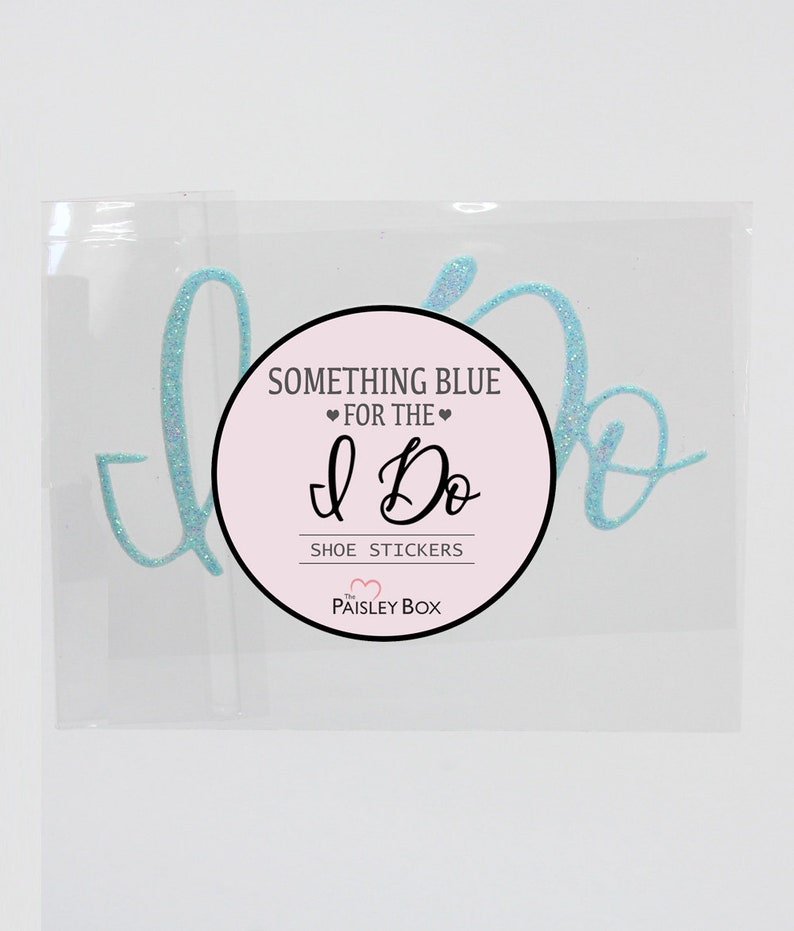 May include: A clear plastic bag containing a pair of light blue glitter shoe stickers that say "I Do". The stickers are packaged with a pink and white circle sticker that says "Something Blue for the I Do Shoe Stickers The Paisley Box".
