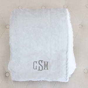 May include: A soft, gray and white sherpa throw blanket with the monogram "GSM" embroidered in the center.