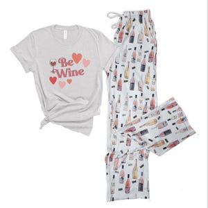 May include: A gray t-shirt with the text "Be Wine" and pink hearts. Matching white pajama pants with a pink wine bottle print.