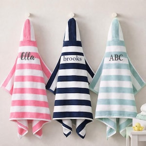 May include: Three hooded towels with horizontal stripes in pink, navy blue, and light green, each featuring white stripes and a personalized name or initials embroidered in dark gray script or block lettering: Ella, brooks, and ABC.